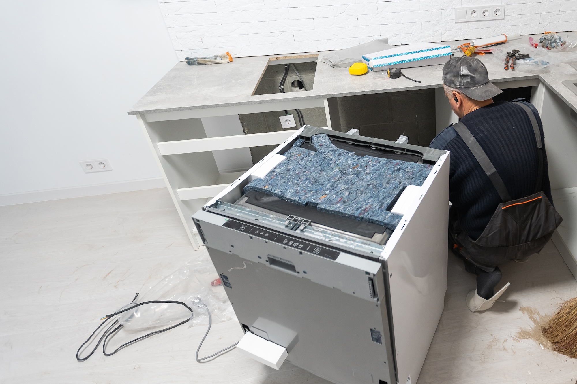 Young Repairman Service Worker Repairing Dishwasher Appliance In Kitchen.